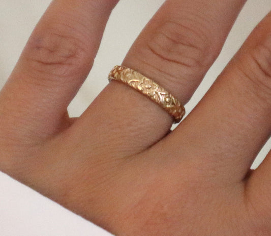 Hand wearing a gold ring with a plain background