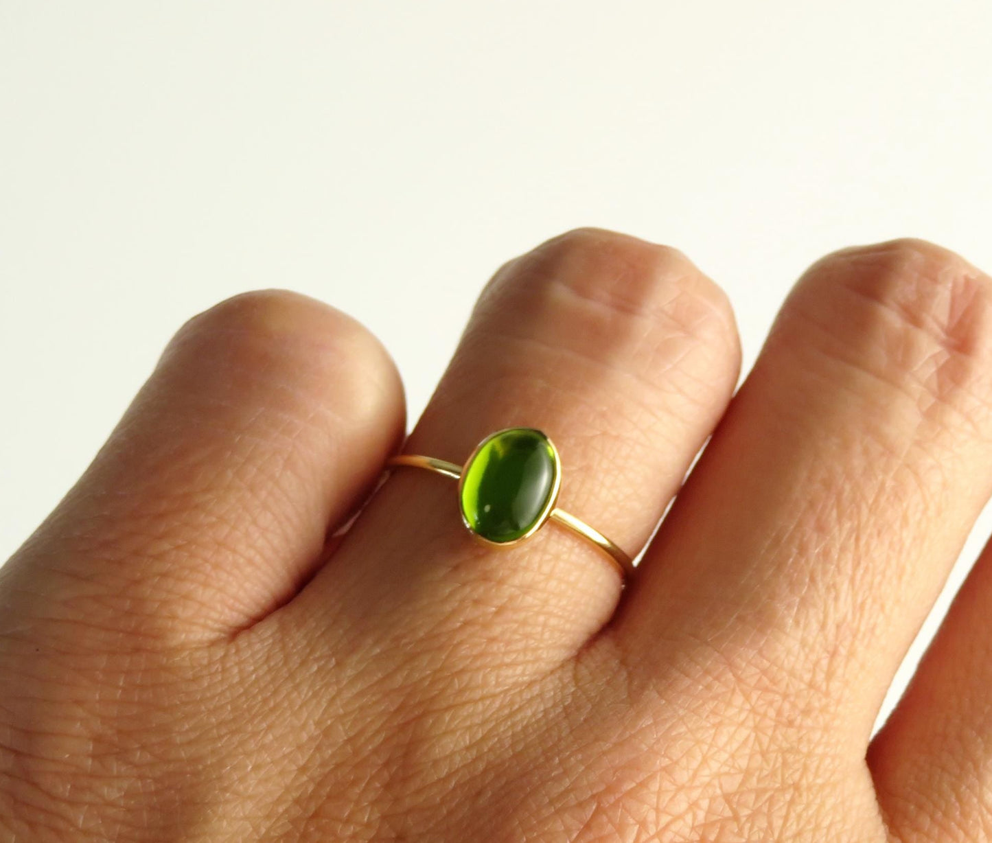 Hand wearing a gold ring with a green gemstone on a white background